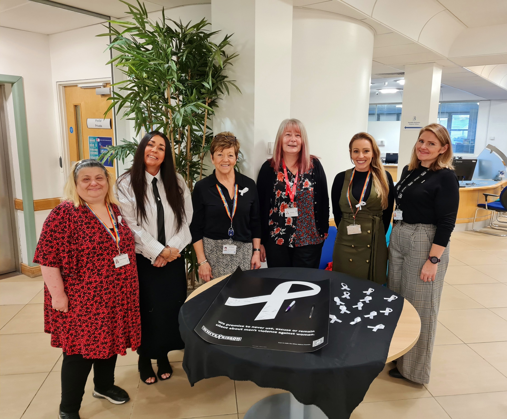 (ch i dd): Dawn Llewellyn, Gwasanaeth Cwsmeriaid (BCBC), Kimberley Coles and Helen Moses, Assia DAS, Jane Gebbie, Cynghorydd a Dirprwy Arweinydd y Cyngor, Zoe Edwards, Rheolwr Ymgynghori, Ymgysylltu a Chydraddoldebau (BCBC) a Kirsty Williams, Rheolwr Partneriaethau a’r Bartneriaeth Diogelwch Cymunedol (BCBC), yn annog pobl i lofnodi addewid y Rhuban Gwyn i #NewidYStori.