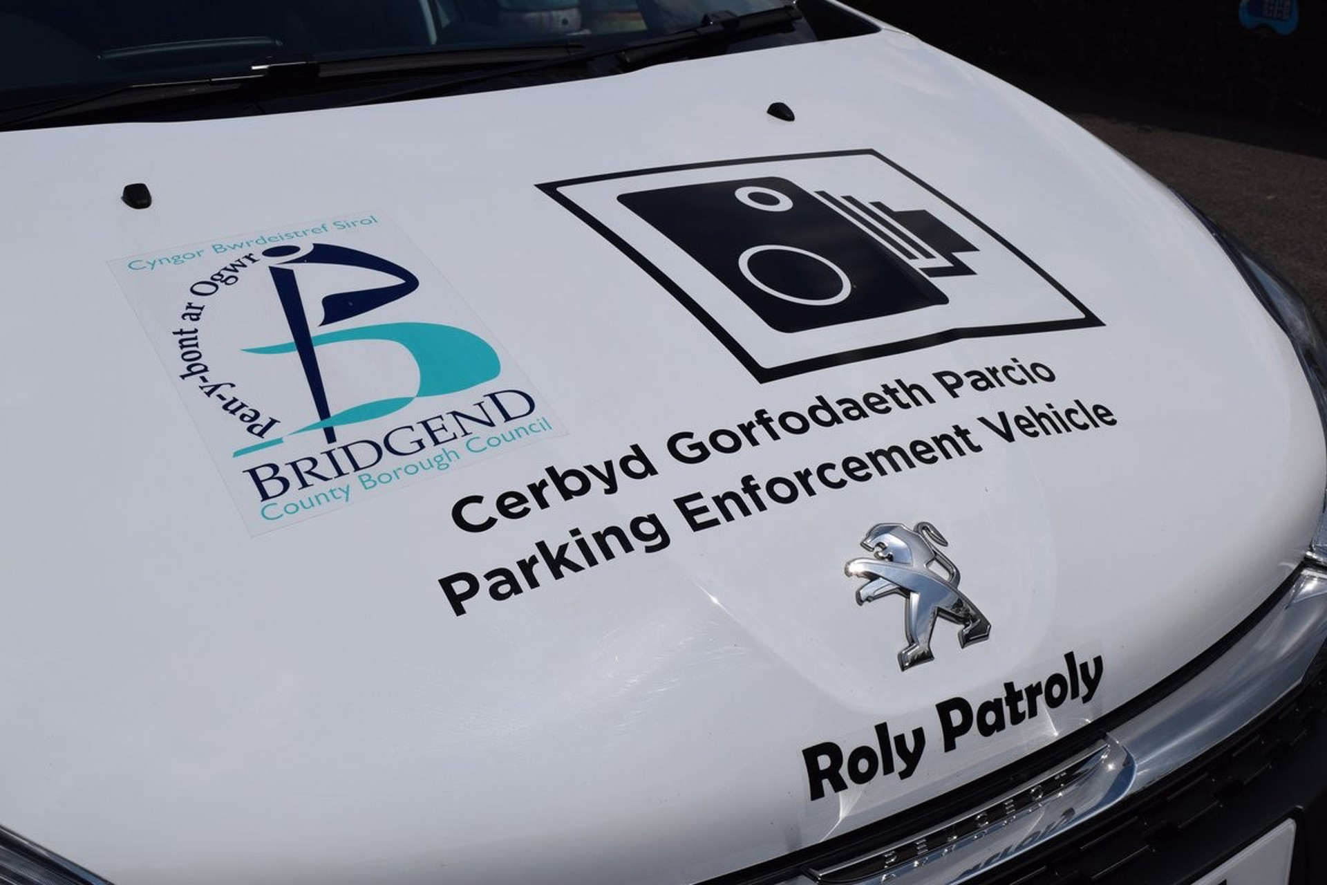 Bonet blaen y car goruchwylio ‘Roly Patroly’ sy’n dangos logo’r cyngor, arwydd camera traffig a’r geiriau ‘Parking Enforcement Vehicle’.